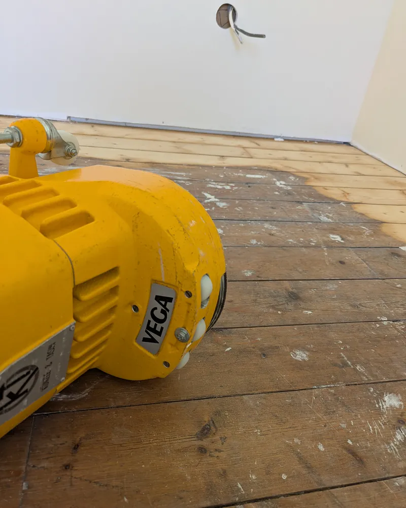 Bordureuse jaune posée sur un parquet près d’un mur.