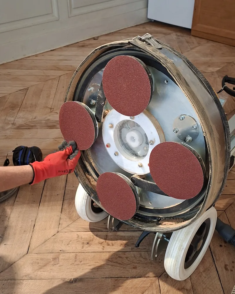 Dessous de la ponceuse planétaire avec ses disques abrasifs rouges.