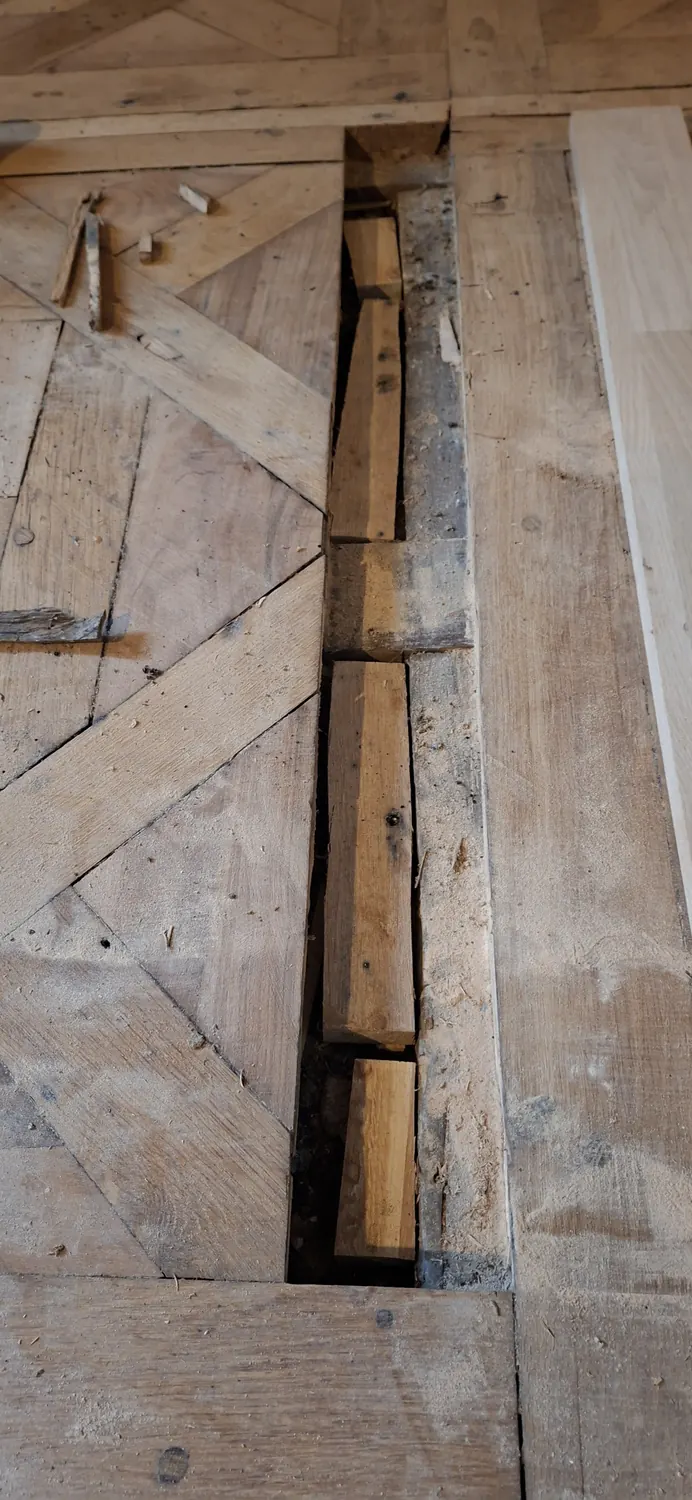 Avant : un gros trou ouvert dans un parquet ancien, les solives apparentes.