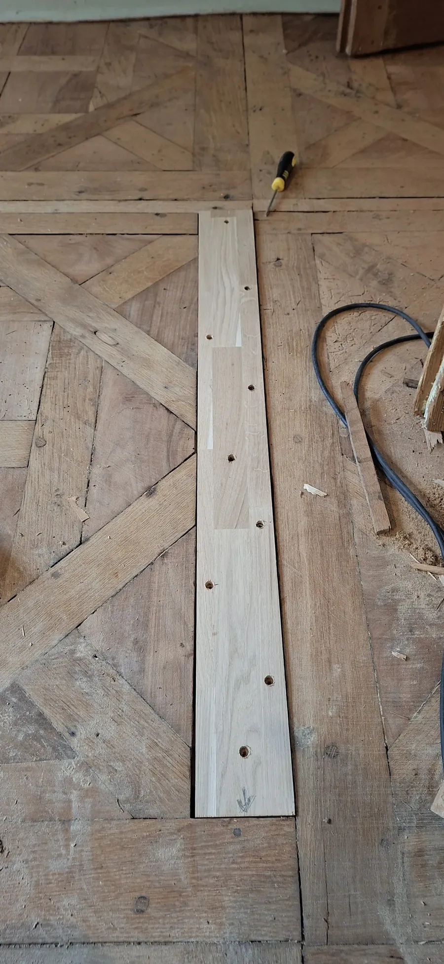 Lame de chêne neuve posée sur un parquet ancien, avant le remplacement des lames abîmées.