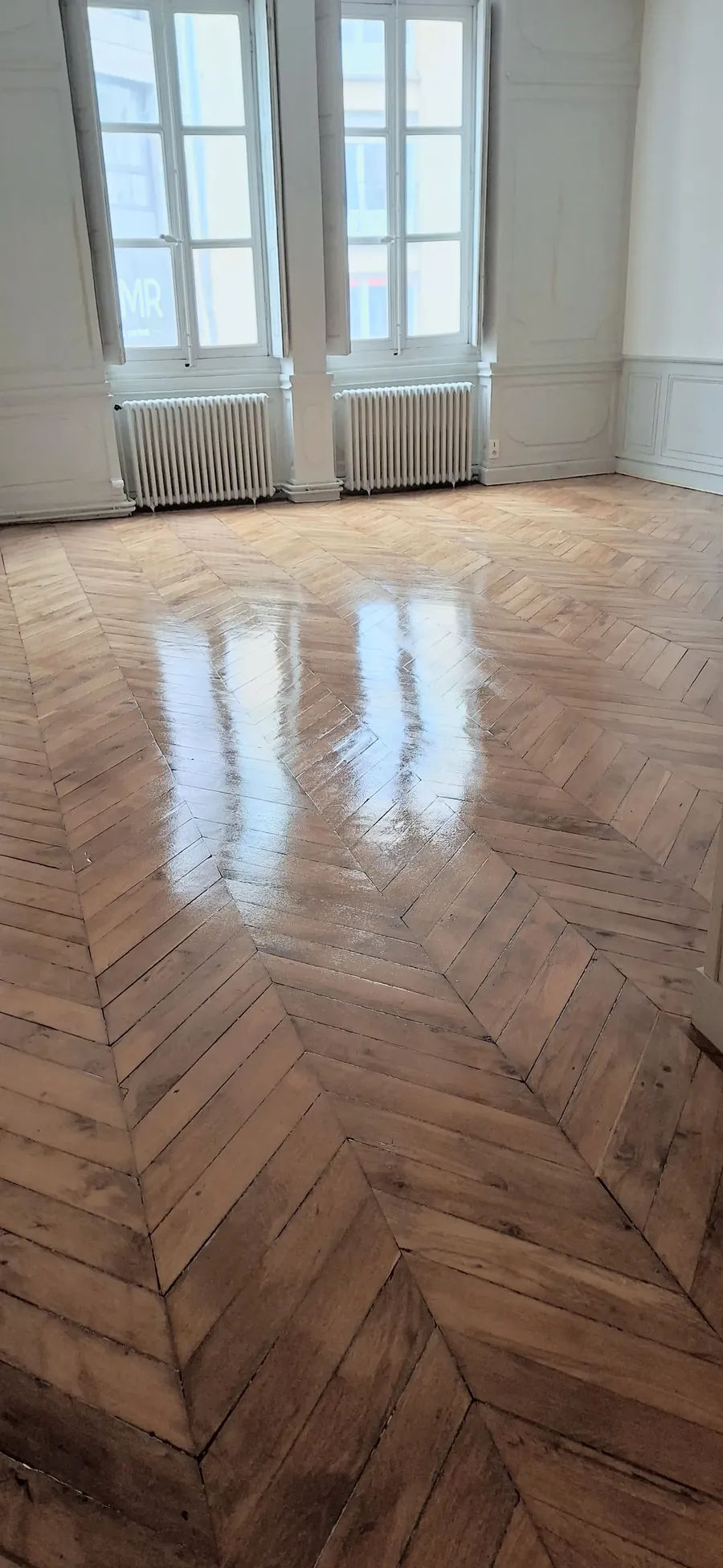 Parquet en chevrons vitrifié, avec les reflets des fenêtres sur le sol.